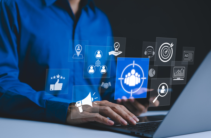 Profesional trabajando en un portátil rodeado de iconos de marketing digital: segmentación de audiencia, diana, megáfono, valoraciones, analítica y atención al cliente